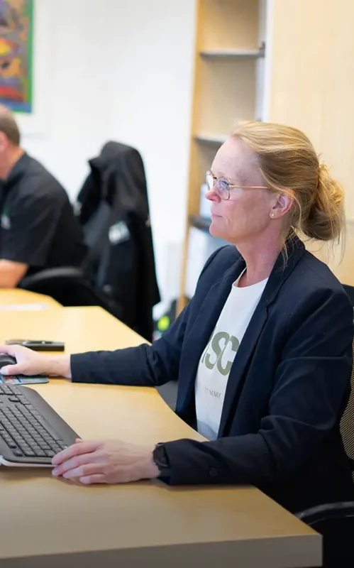En kvinde med briller og blazer, der arbejder ved en computer på et kontor